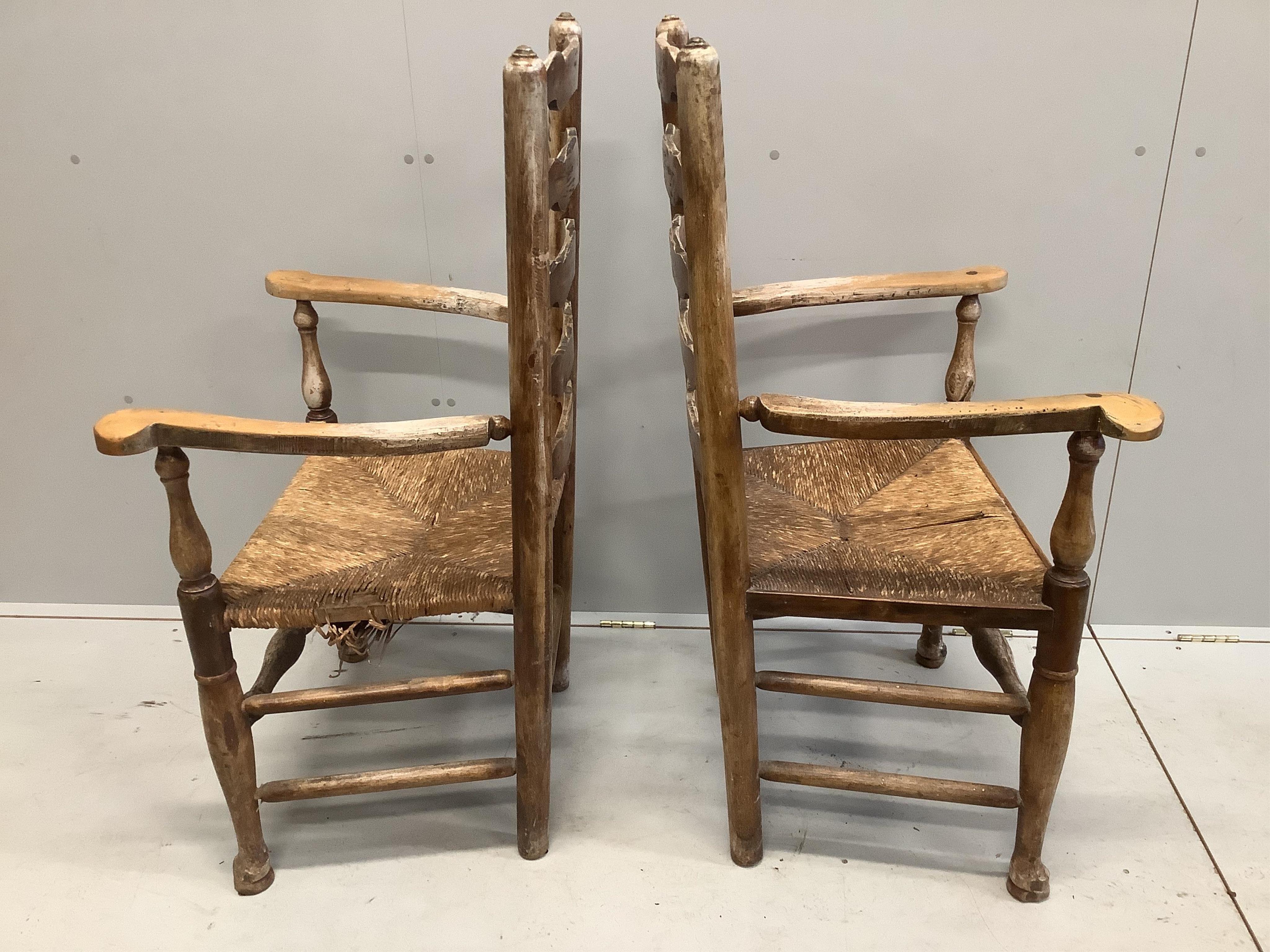 A pair of 19th century Provincial fruitwood rush seated ladder back elbow chairs, later painted, width 64cm, depth 48cm, height 112cm. Condition - poor to fair